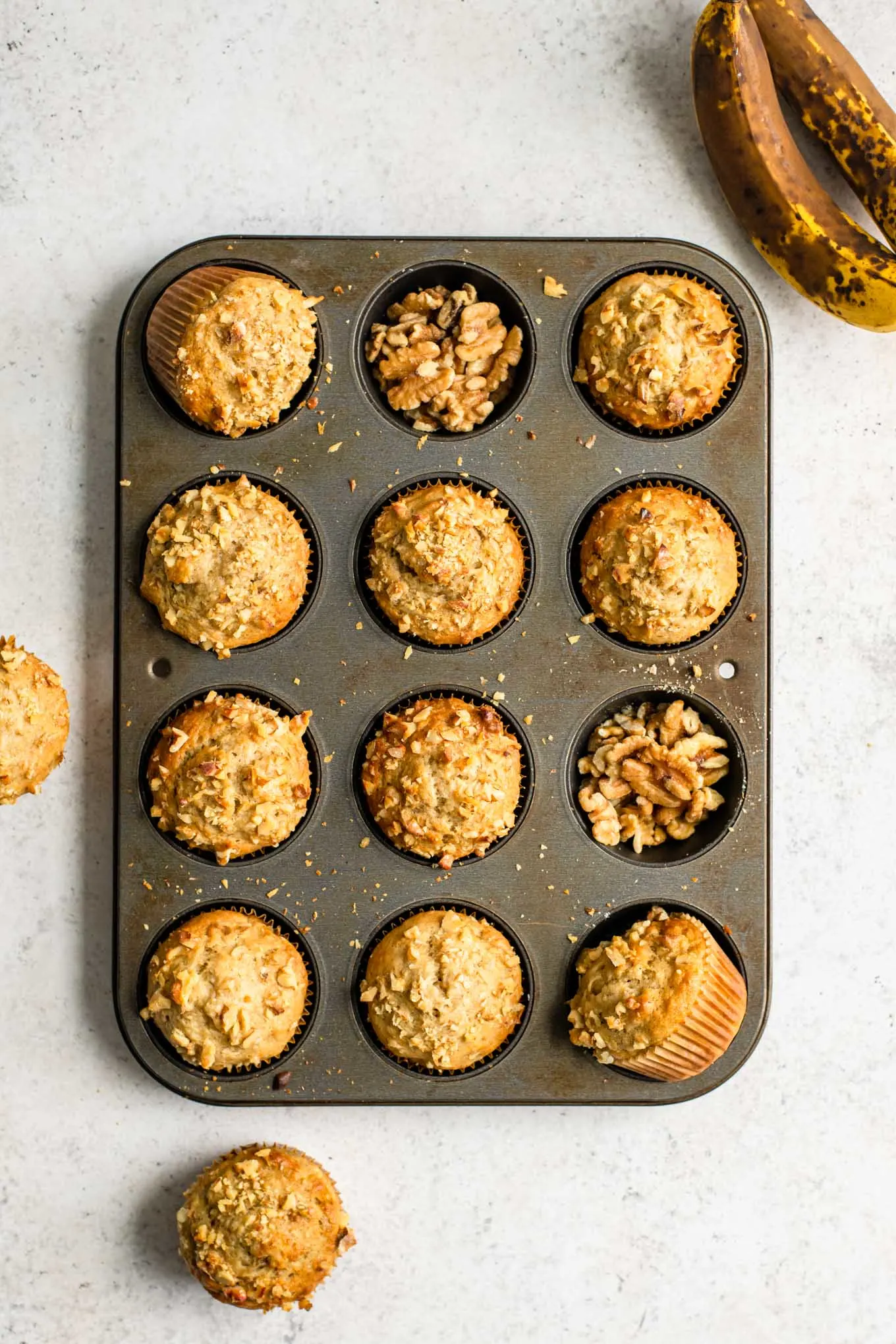 baked banana nut muffins in a muffin pan with two of the muffin wells filled with walnuts