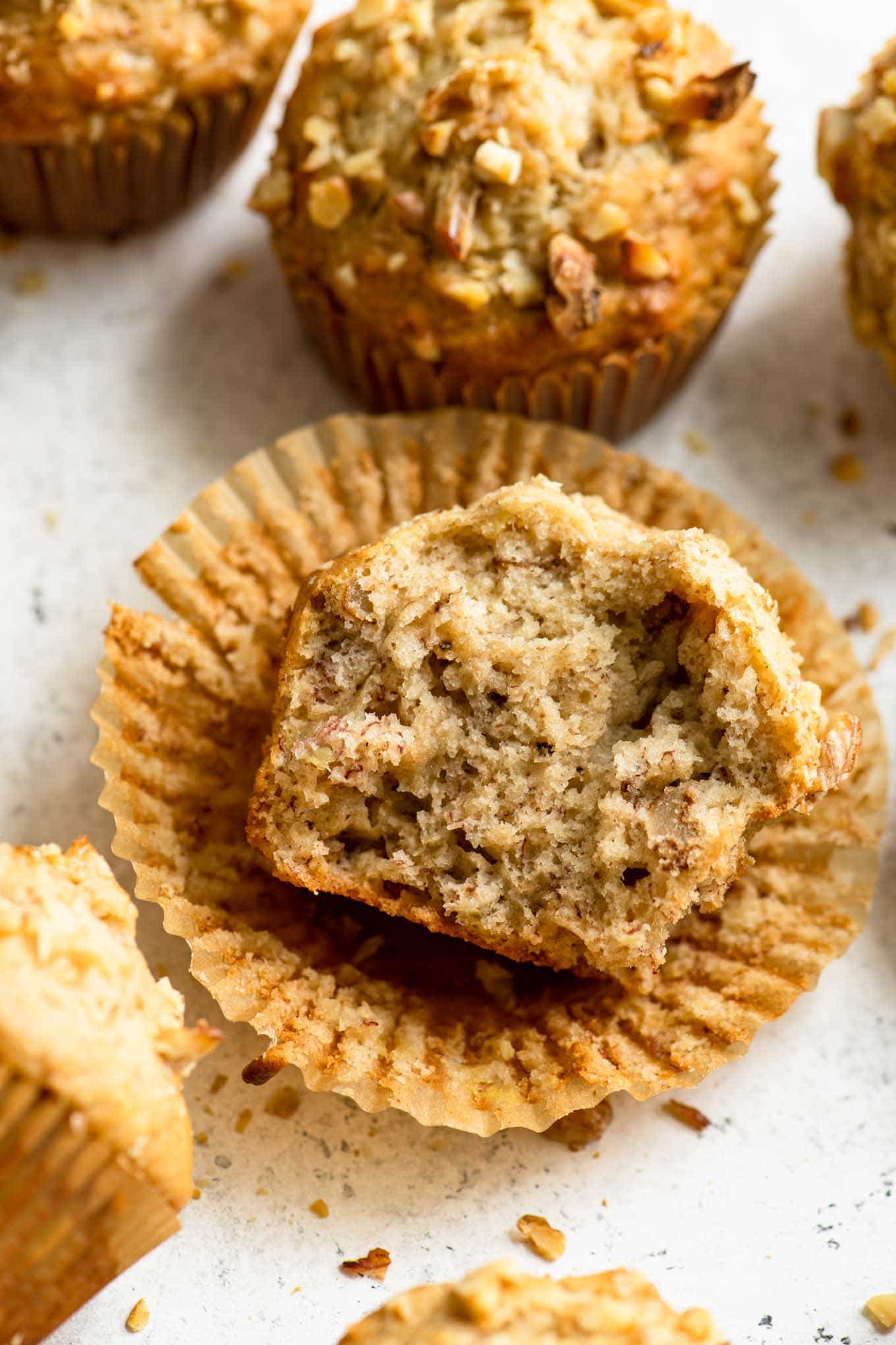 angled view of vegan banana nut muffin unwrapped and broken in half to show the soft crumb