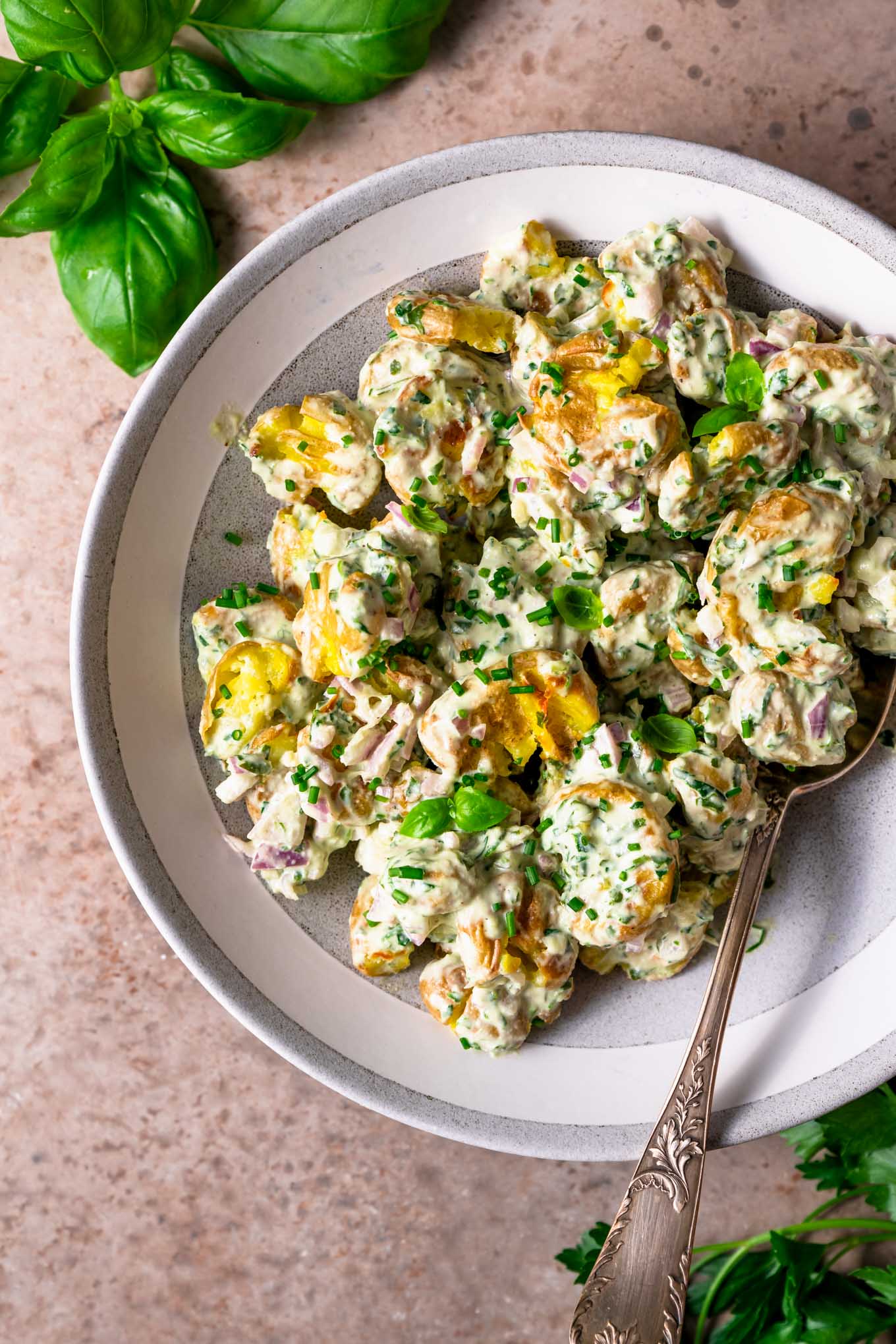 herbed smashed potato salad in bowl with basil and parsley sprigs in edge of photo