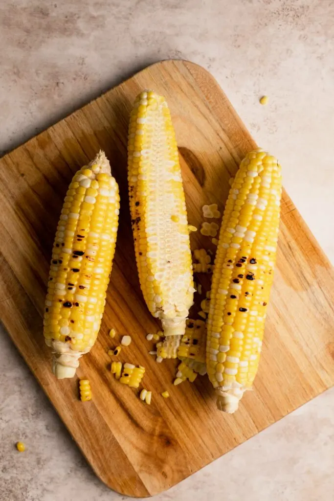 roasted corn on the cob on a cutting board with kernels cut off one side of one cob