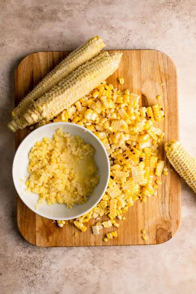 corn cut off cobs on cutting board with bowl full of kernels and juice scraped off cobs