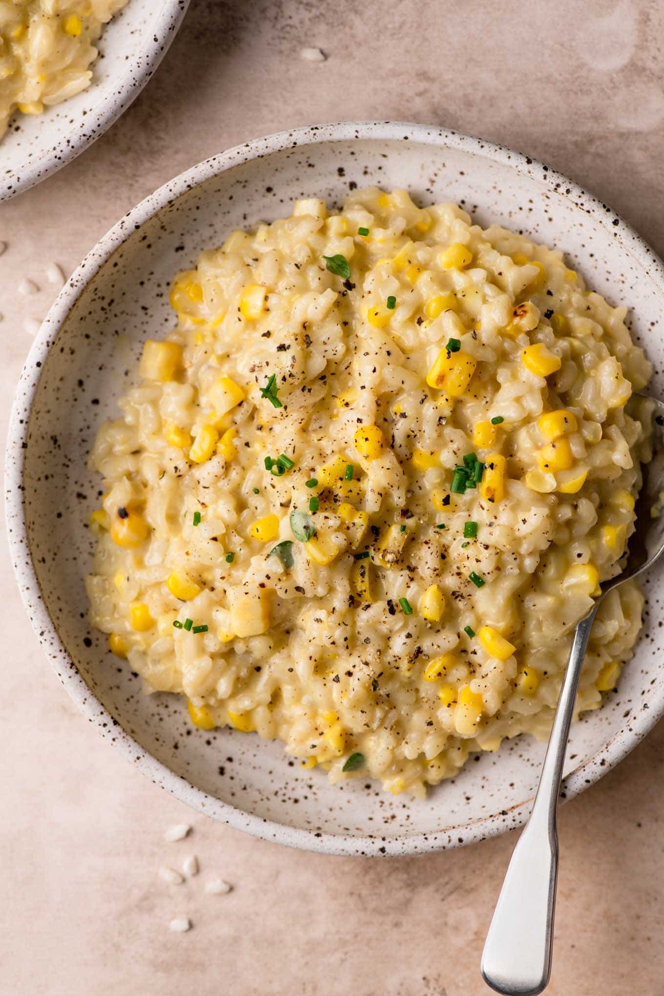 sweet corn risotto in a bowl topped with chives and black pepper