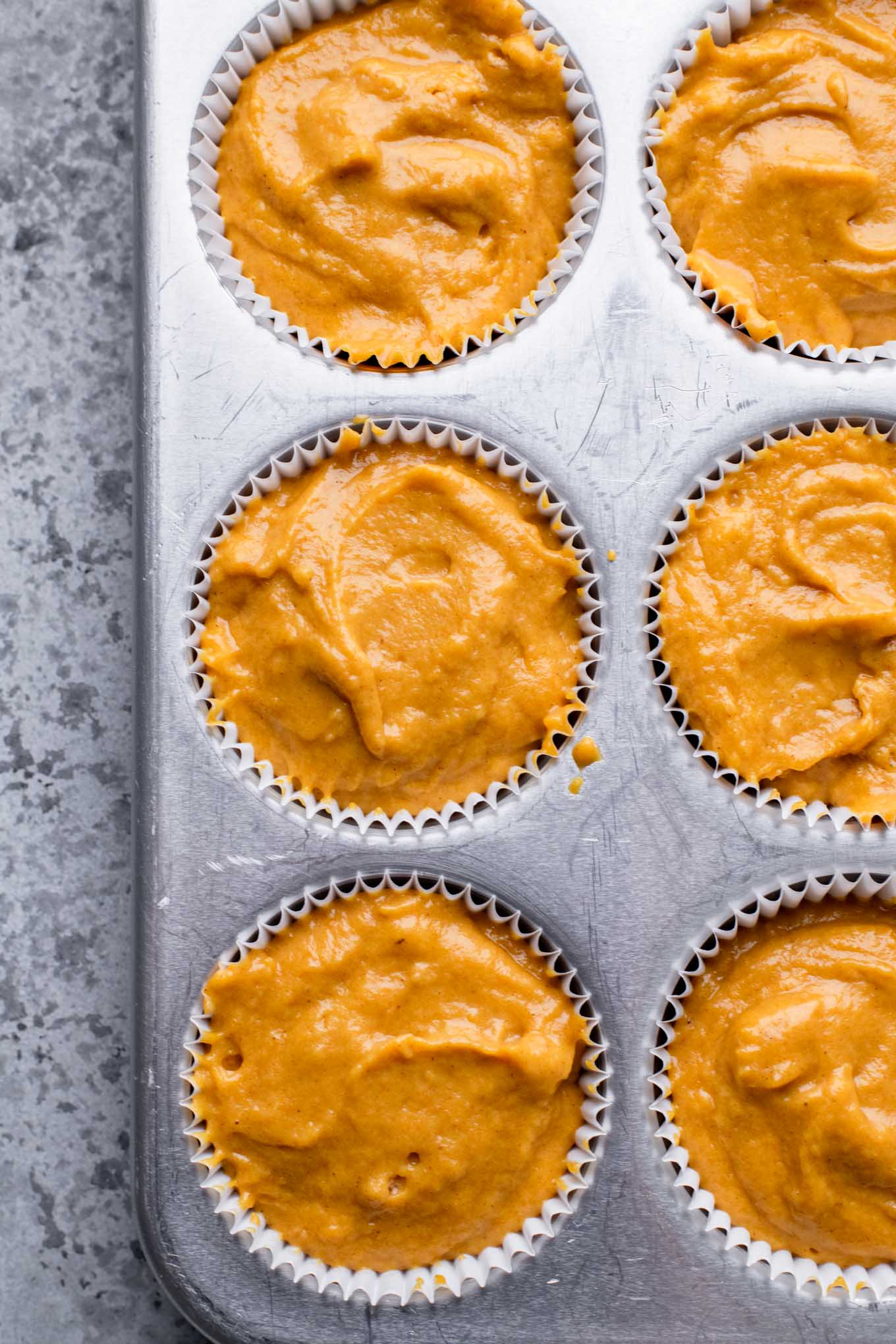 pumpkin muffin batter in lined muffin tins, filled almost to the top