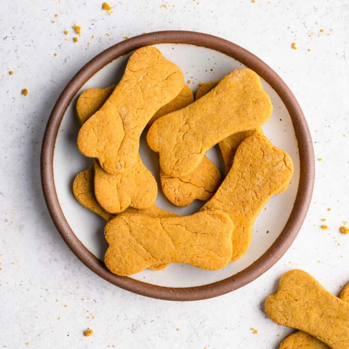 peanut butter pumpkin dog treats on a plate with crumbs surrounding plate