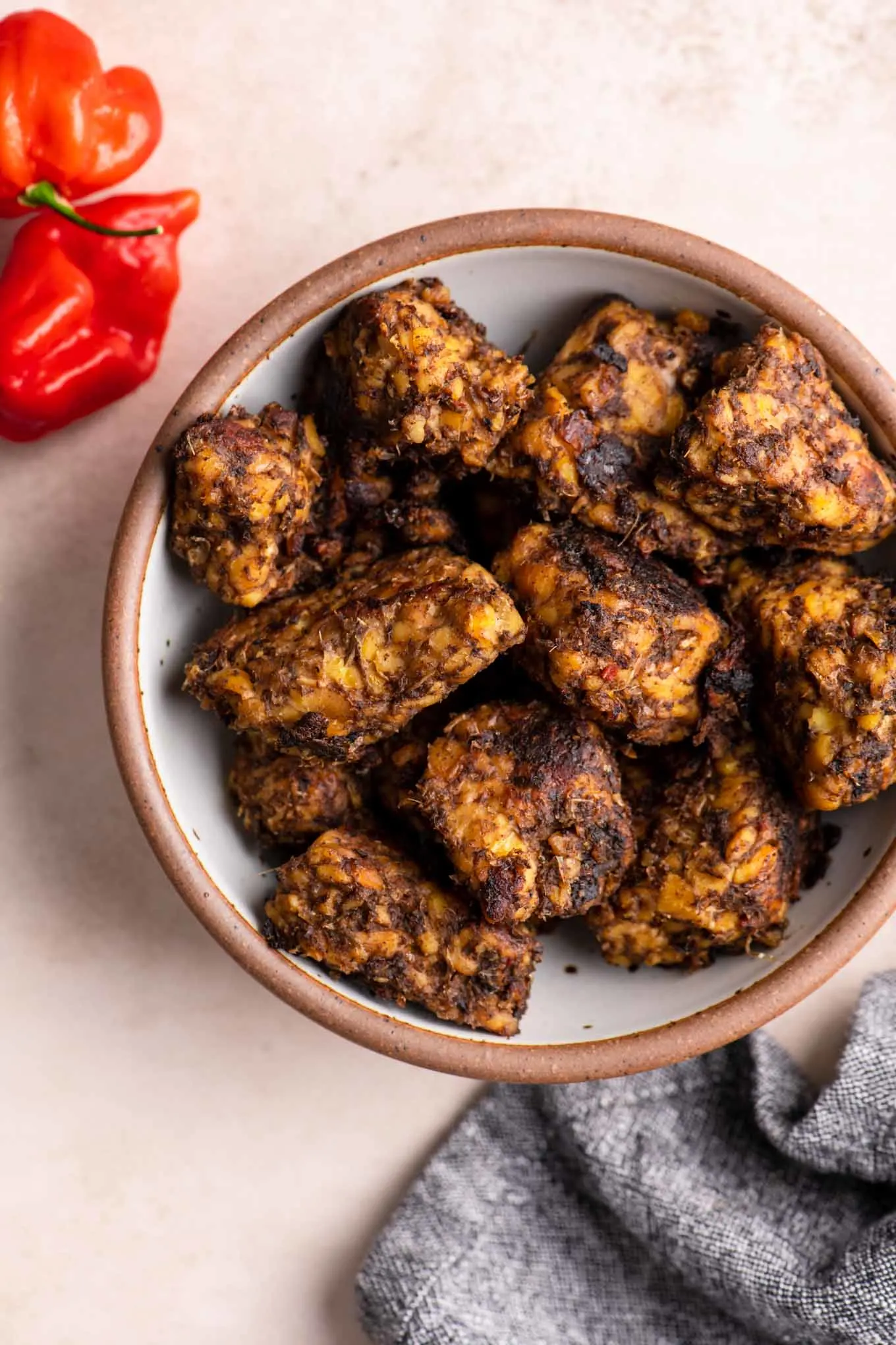 jamaican jerk tempeh in a bowl with two scorpion peppers on the side