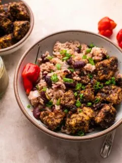 Jamaican jerk tempeh served with red beans and rice in a bowl with a small bowl of jerk tempeh on the side