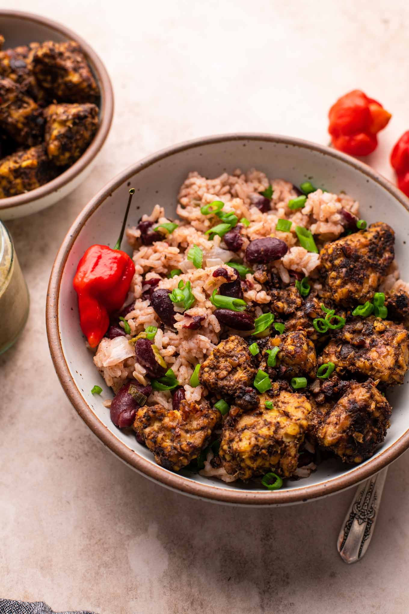 Jamaican jerk tempeh served with red beans and rice in a bowl with a small bowl of jerk tempeh on the side