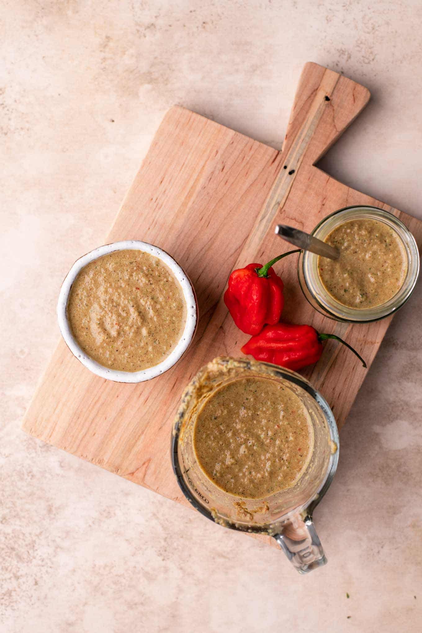 jerk sauce in measuring cup and jar with two peppers on cutting board