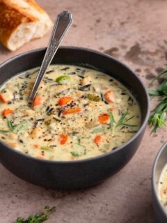 vegan white bean and wild rice soup in a bowl with sprigs of thyme and tarragon as garnish