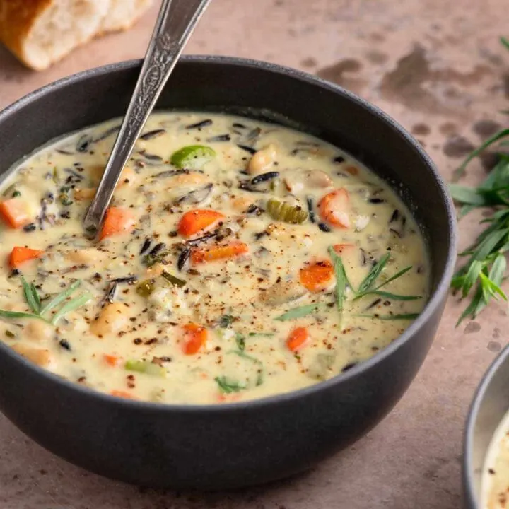 vegan white bean and wild rice soup in a bowl with sprigs of thyme and tarragon as garnish