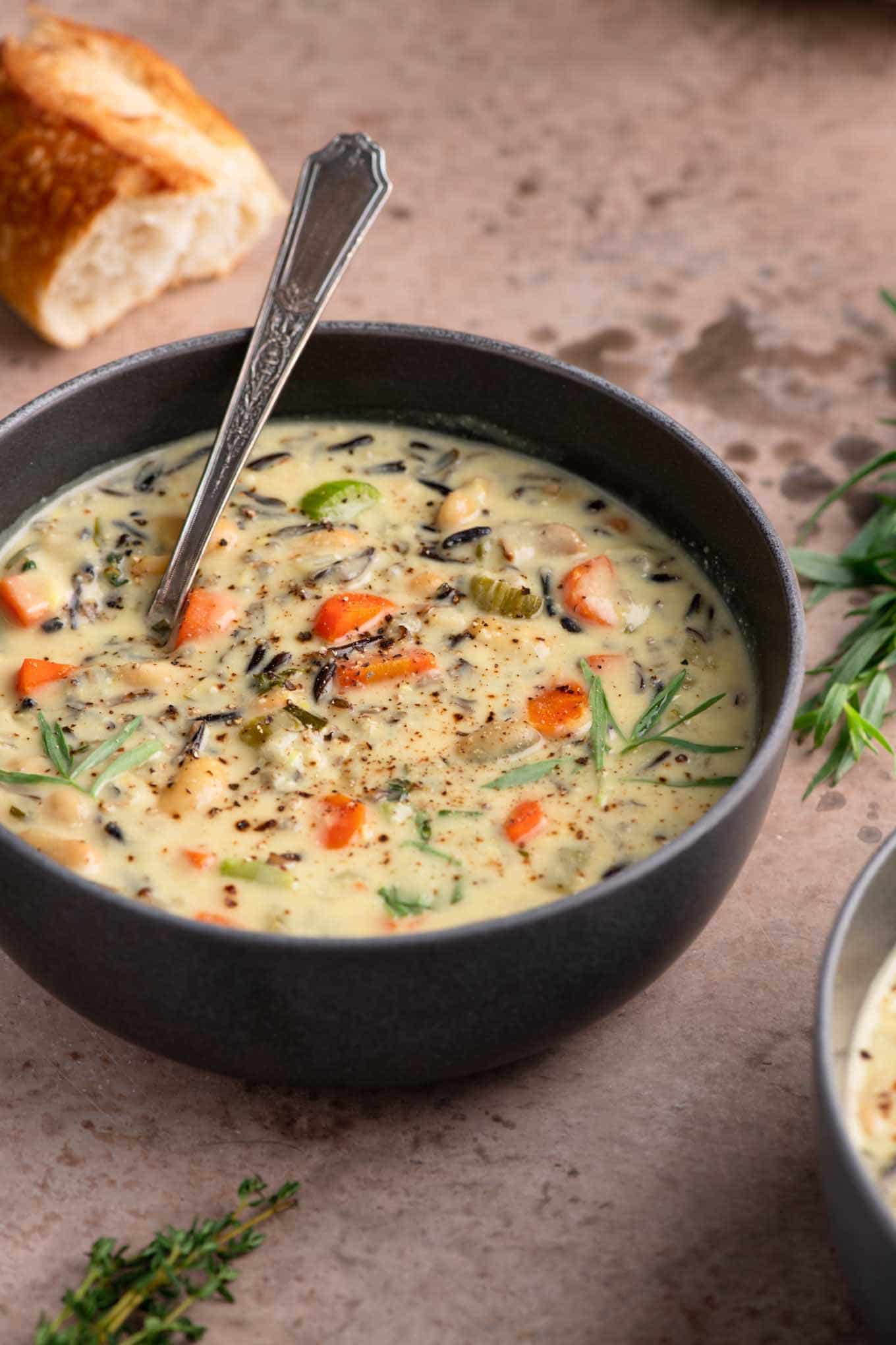 vegan white bean and wild rice soup in a bowl with sprigs of thyme and tarragon as garnish