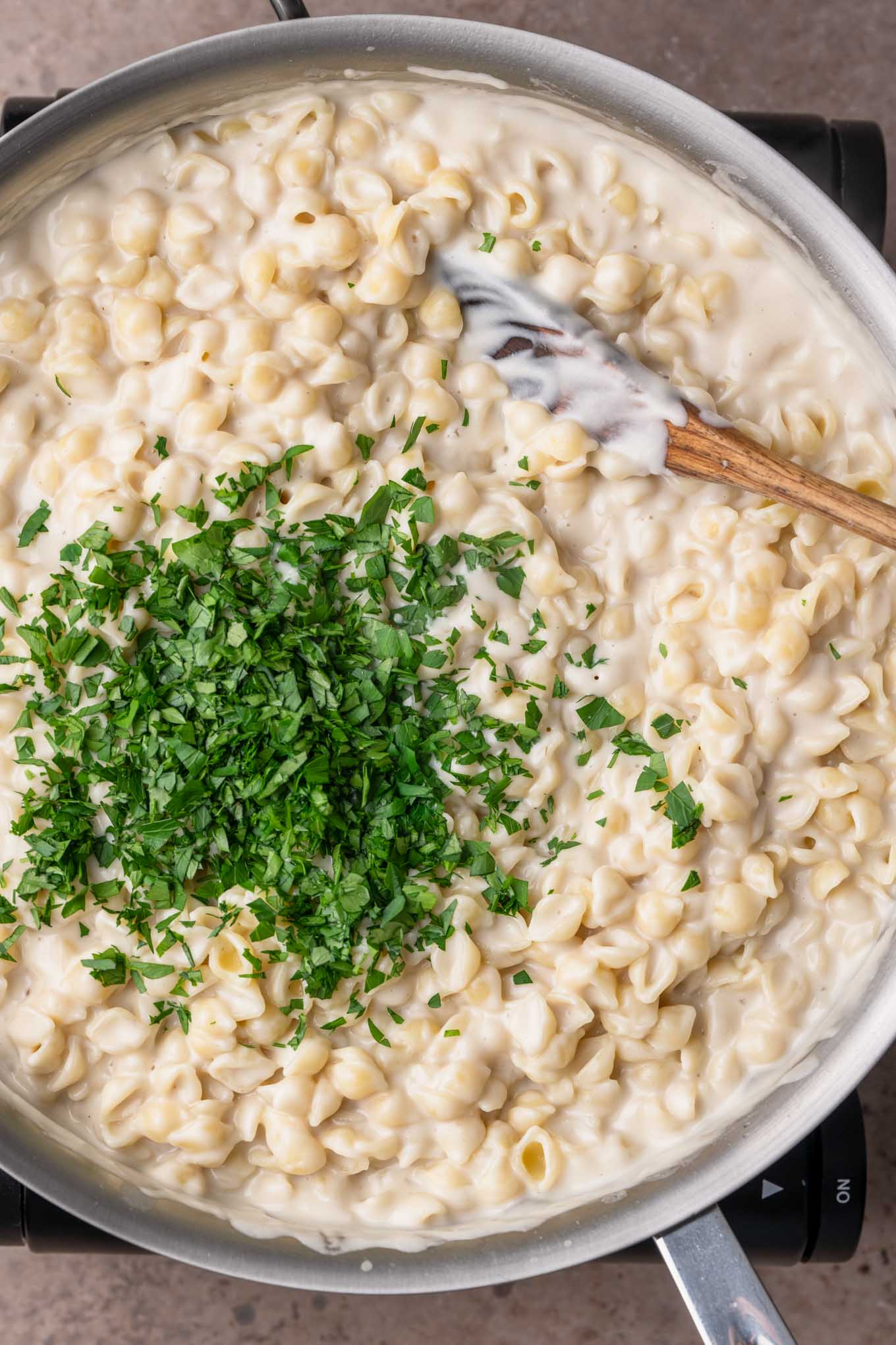 mini shells, creamy garlic sauce, and minced parsley in a pot being stirred together