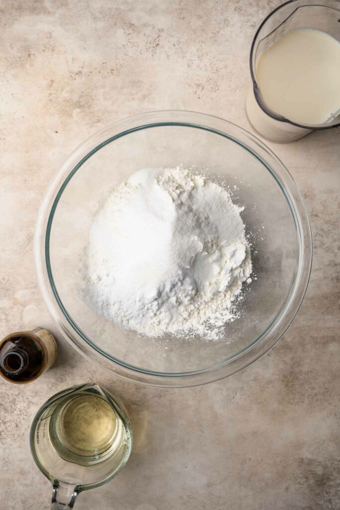 dry ingredients in a mixing bowl with oil and milk measured out and a bottle of vanilla extract