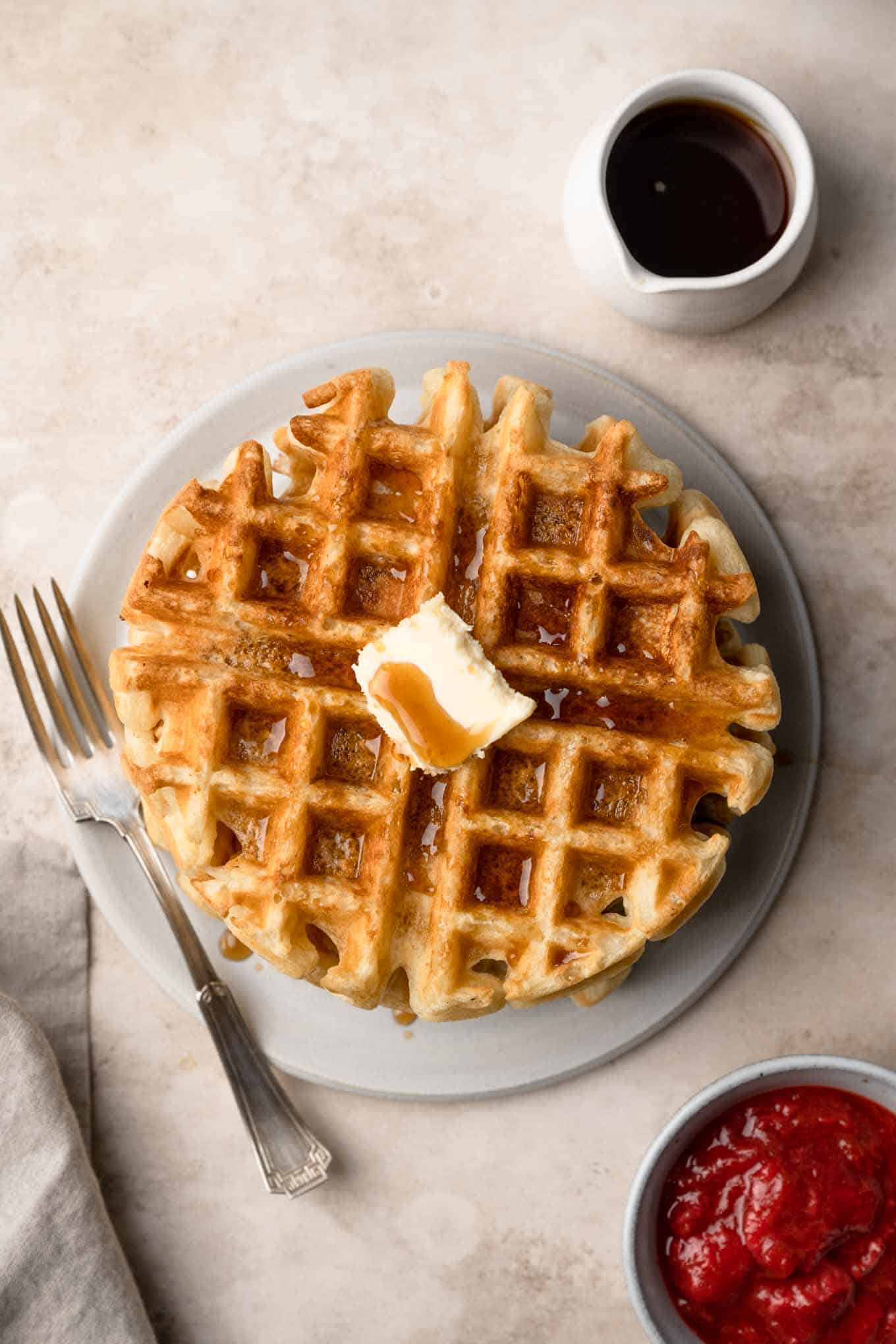 overhead shot of a vegan waffle on a plate topped with maple syrup and a side of berry compote