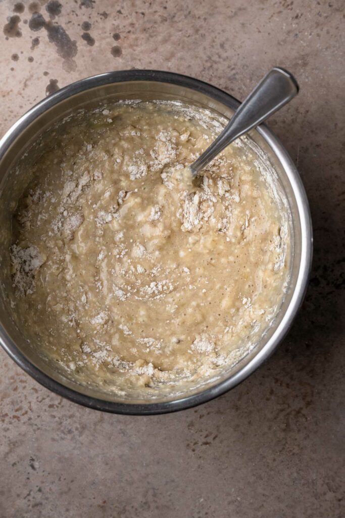 dry ingredients and wet ingredients for banana bread mixed together in a mixing bowl until mostly combined with some clumps of flour