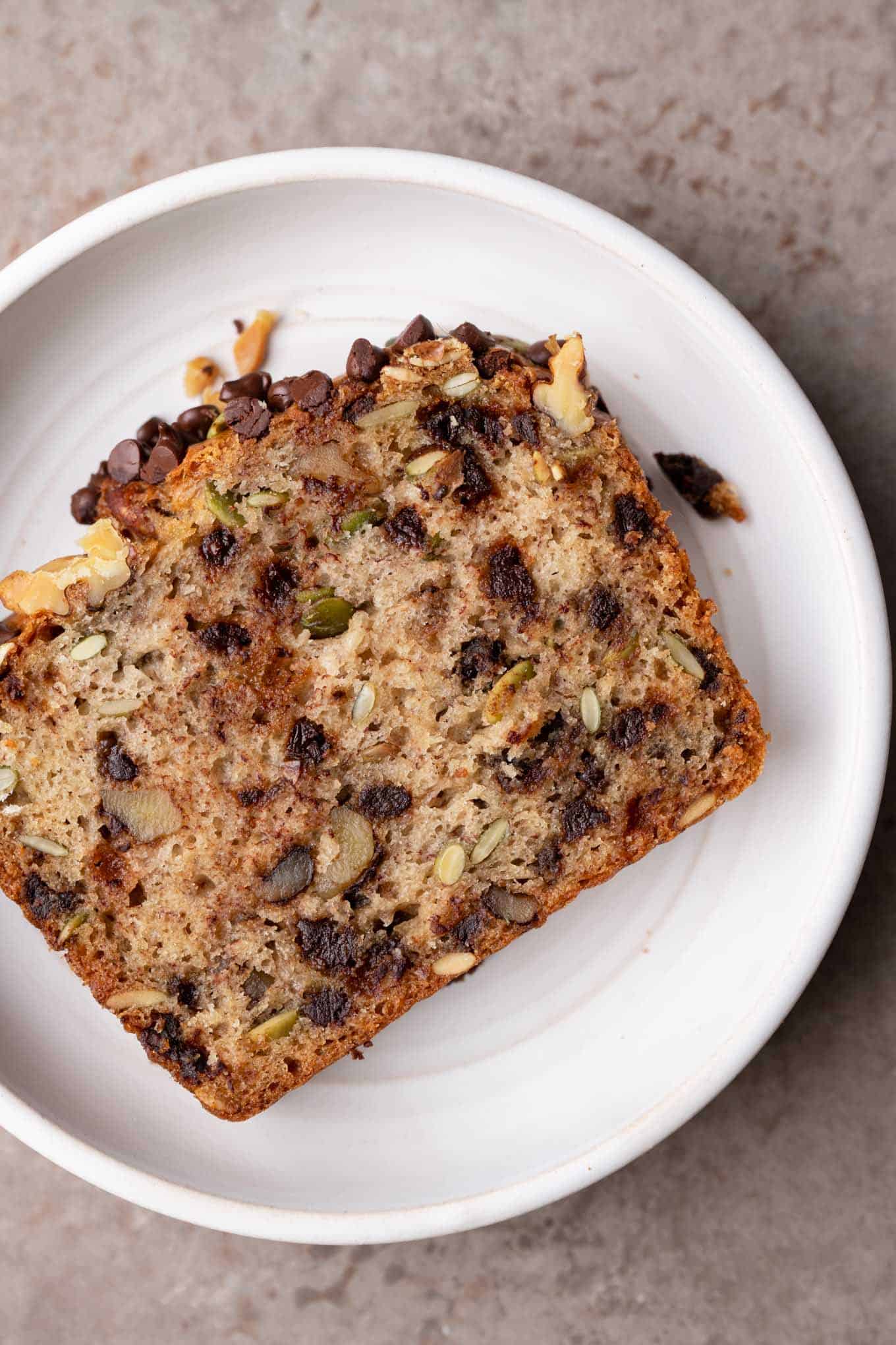 close up shot of a slice of chocolate chip, walnut, pepita banana bread on a plate